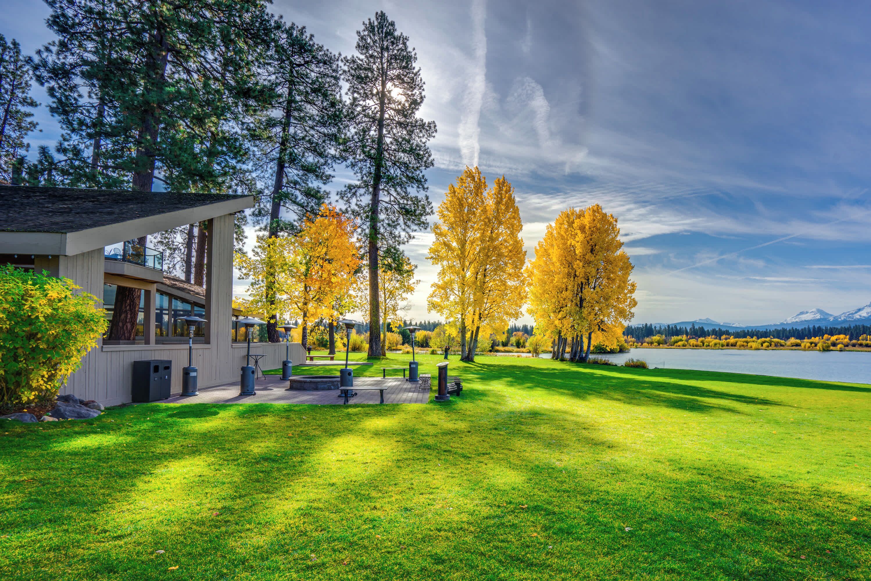 Une maison moderne dotée d’un patio, d’un lac et entourée d’arbres aux couleurs automnales.