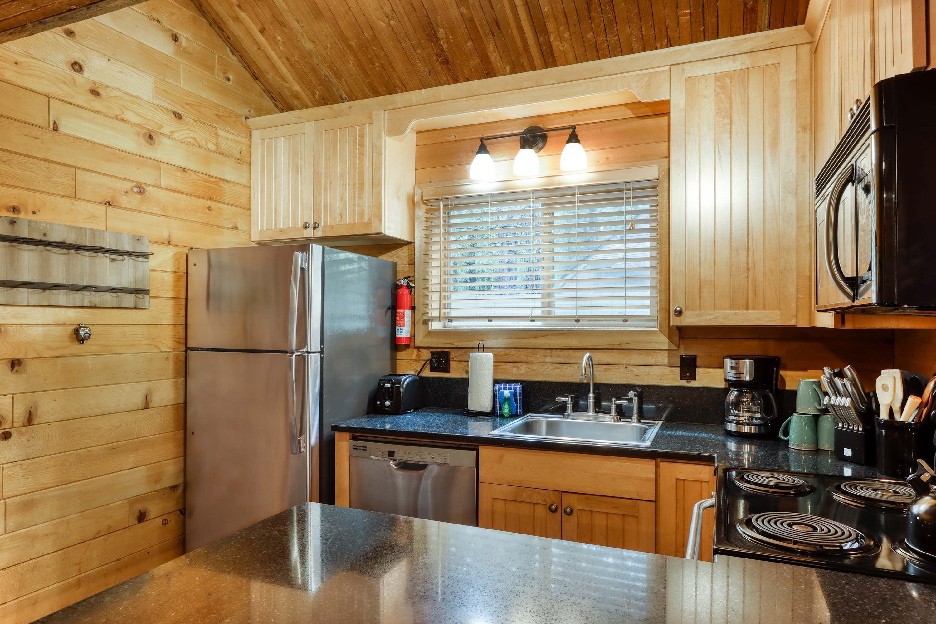 A kitchen with wooden cabinets, a stainless steel refrigerator, a dishwasher, a stove, and a sink with a window above.