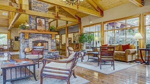 A spacious living area with a stone fireplace, wooden beams, and large windows. - Cozy condo with shared pool, hot tub, sauna, fitness room, washer and dryer (Bend)
