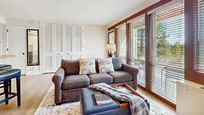 A living room with a sofa, a coffee table, and a dining area with a bar stool. - Cozy condo with shared pool, hot tub, sauna, fitness room, washer and dryer (Bend)
