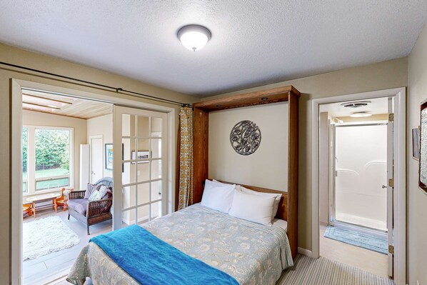 Ein Schlafzimmer mit Bett, Fenster, Tür und Blick ins Freie.