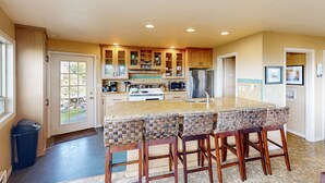 Una cocina con una isla central, taburetes de bar, armarios de madera y un refrigerador de acero inoxidable.