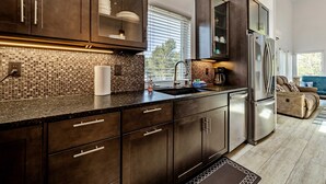 A modern kitchen with dark cabinetry, a stainless steel refrigerator, and a window with blinds.