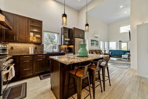A modern kitchen with dark wood cabinets, a granite countertop, and bar stools. - Stunning apt near the ocean with gas fireplace, partial water views & grill (Gold Beach)