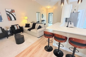A modern living room with a sofa, a coffee table, and a bar area with stools. - 15 Minutes to Disney Theme Parks. Heated pool. (Kissimmee)