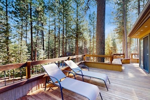 A deck with lounge chairs, surrounded by tall trees, and a building with large windows. - Tree-lined home with private hot tub, 7 pools, 14 tennis courts, golf, gym, AC (Black Butte Ranch)