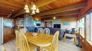 A wooden interior with a dining table, chairs, a kitchen area, and a seating area with a TV and lamp. - Oceanfront, Dog-Friendly Home with Fireplace, Ocean View, Beach Access & WiFi (Yachats)