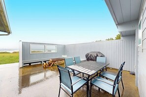 En täckt uteplats med ett bord och stolar, en grill och utsikt över havet.