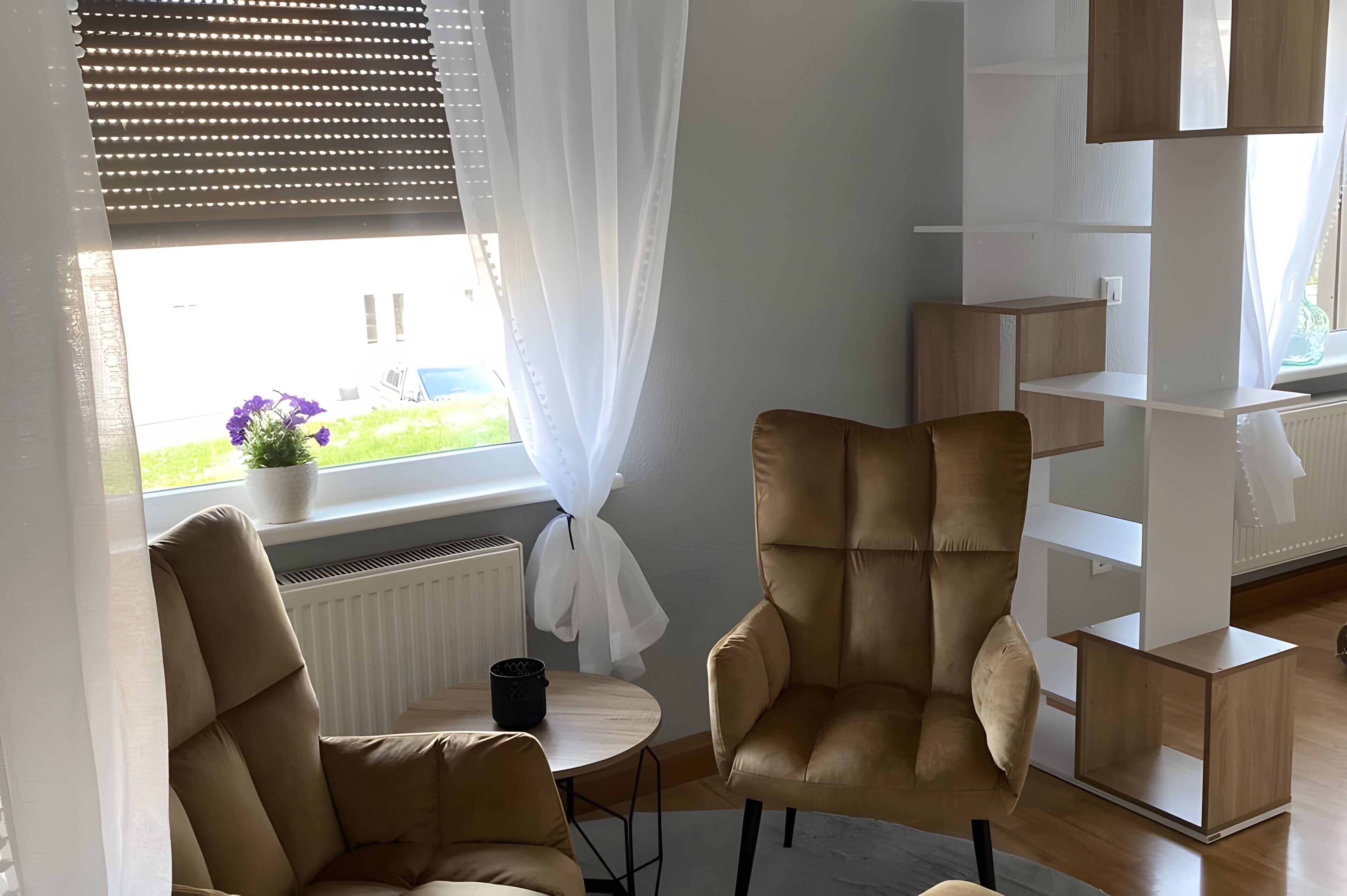En moderne stue med en sofa, en lænestol, et lille bord og et hvidt reolsystem.
