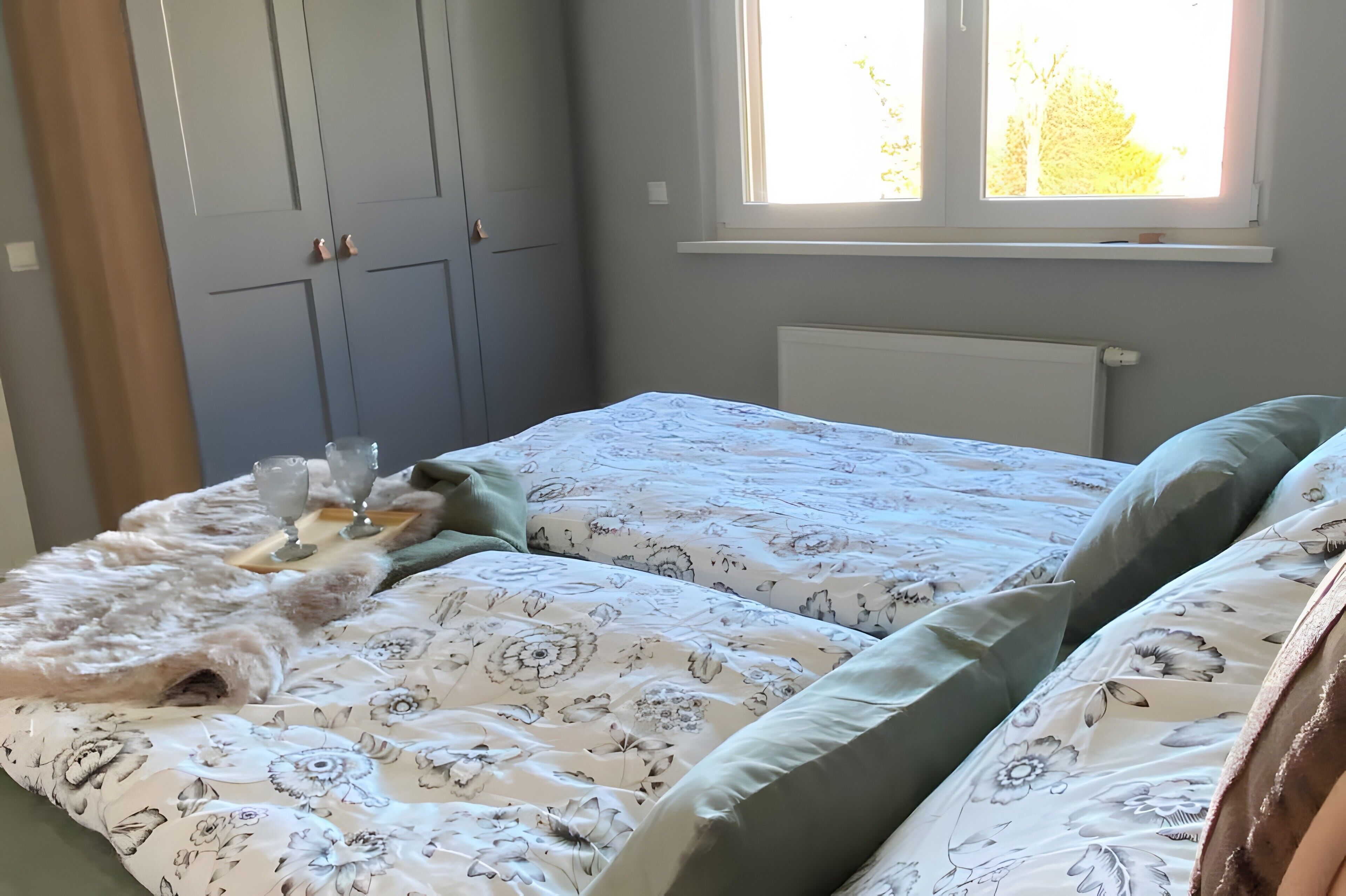 A bedroom with two beds, a wardrobe, a window, and a radiator.