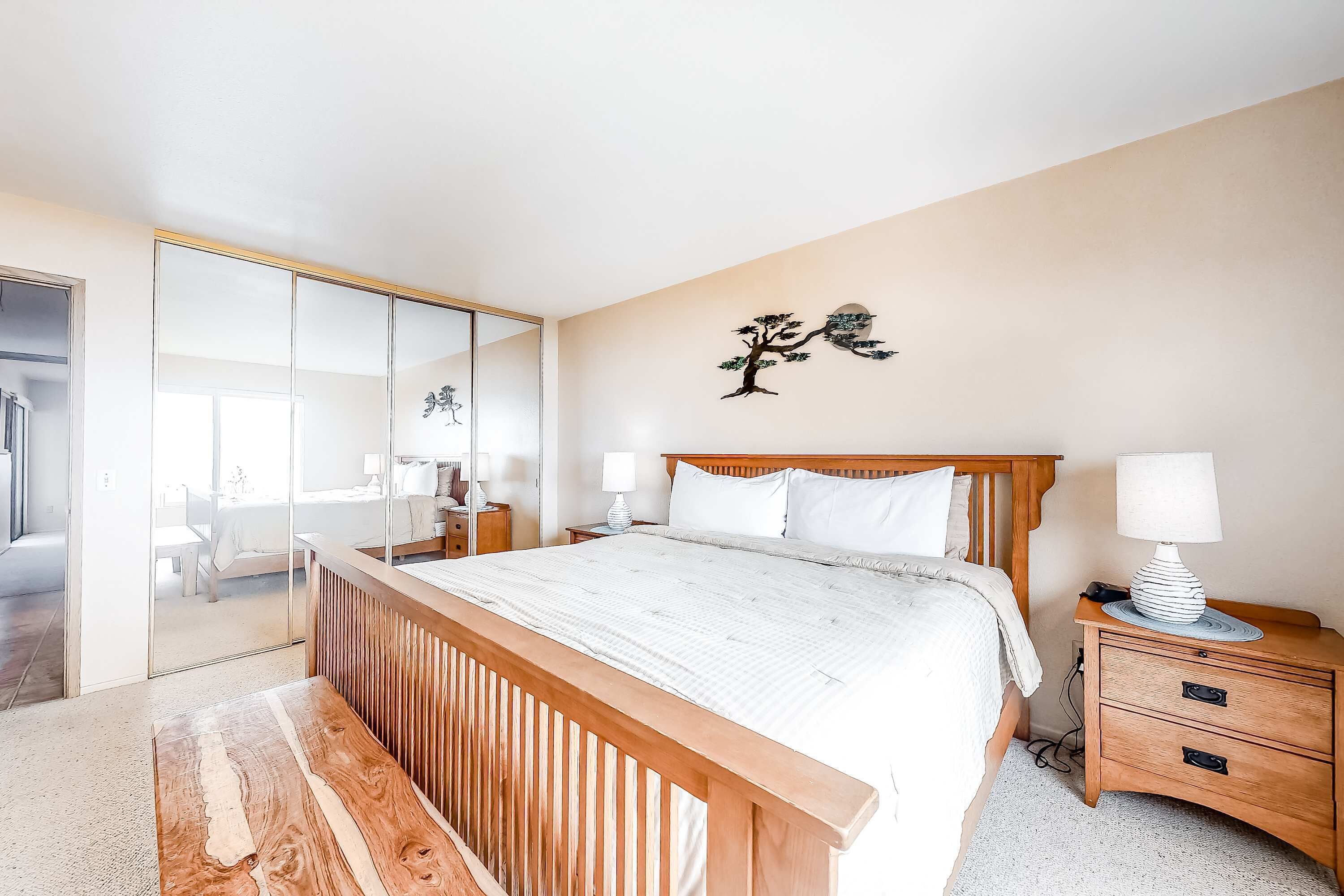 Une chambre à coucher comprenant un lit, des tables de chevet, un miroir et une œuvre d’art murale.