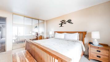 Une chambre à coucher comprenant un lit, des tables de chevet, un miroir et une œuvre d’art murale.