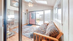 En stue med sofa, glasdør til en patio, loftventilator og stort vindue.