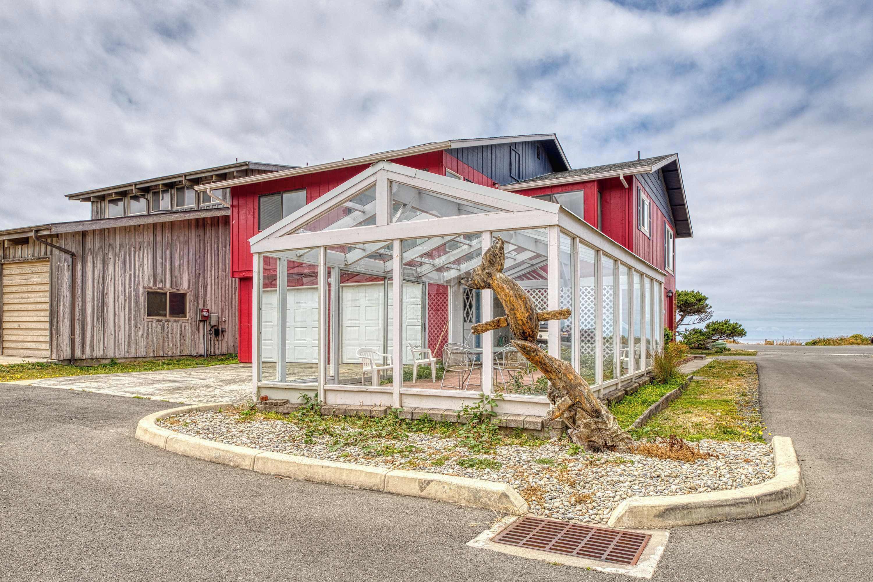 Une maison moderne dotée d’une véranda en verre, d’une terrasse en bois et d’une façade rouge.
