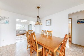 Un coin repas avec une table et des chaises en bois, un luminaire suspendu, une horloge murale et une porte donnant sur une autre pièce.