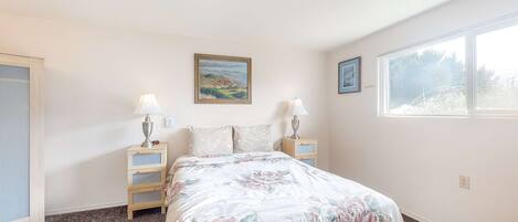 A bedroom with a floral bedspread, two bedside lamps, a nightstand, a framed picture on the wall, and a window with a view.