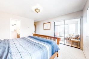 Une chambre à coucher comprenant un lit, un banc en bois, une porte-fenêtre coulissante et un luminaire au plafond.