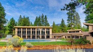 A building with a swimming pool, surrounded by trees and a fence. - Rustic-chic home with patio, pools, hot tubs, & fitness center (Black Butte Ranch)