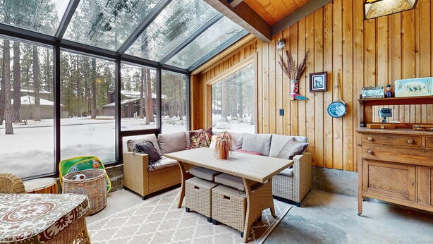 A cozy room with a large glass window, wicker furniture, and a wooden cabinet. - Rustic-chic home with patio, pools, hot tubs, & fitness center (Black Butte Ranch)