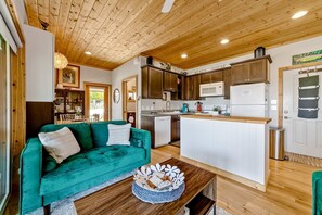 A cozy kitchen with wooden cabinets, a white refrigerator, and a dining area with a green sofa. - Charming coastal home with water views, large covered deck (Gold Beach)