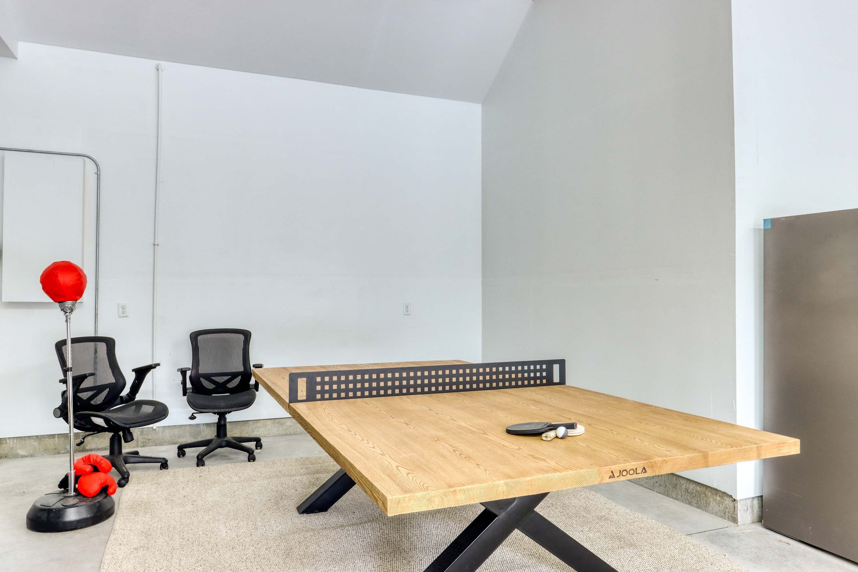 Een vergaderruimte met een houten tafel, zwarte bureaustoelen, een tafeltennistafel en een rode fitnessbal.