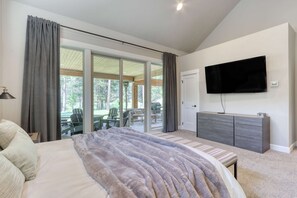 Ein Schlafzimmer mit einem großen Bett, einem Flachbildfernseher, einer Glastür, die zu einem Außenbereich mit Stühlen und einem Tisch führt.