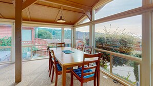 A covered dining area with a table and chairs, large windows, and a view of the surrounding area. - Oceanfront home with private hot tub, walls of glass & spectacular view (Brookings)