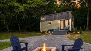 Une petite cabane avec un foyer et deux chaises Adirondack devant.