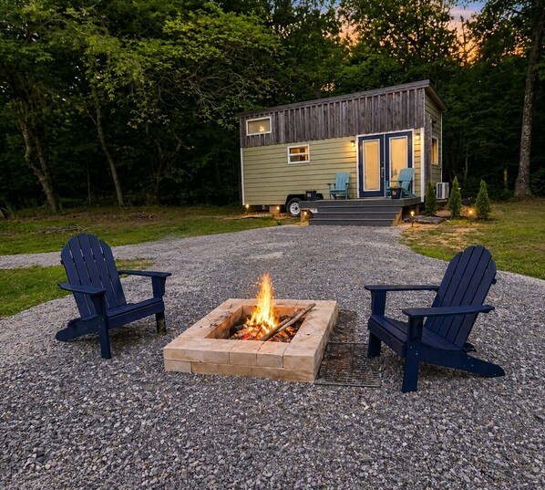 A small cabin with a fire pit and two Adirondack chairs in front.