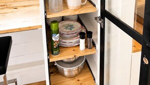 Una cocina con armarios abiertos, un microondas, una cafetera y diverso menaje de cocina.