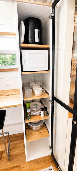 A kitchen with open cabinets, a microwave, a coffee maker, and various kitchenware.
