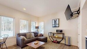 A living room with a sofa, coffee table, TV, and a small table with a globe. - Adorable Bend townhome with ideal location, kitchenette & central AC (Bend)
