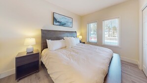 A bedroom with a large bed, two bedside tables with lamps, a wall-mounted artwork, and a window with blinds. - Adorable Bend townhome with ideal location, kitchenette & central AC (Bend)