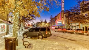 A snow-covered street with a parked SUV, a bench, and a trash can. - Adorable Bend townhome with ideal location, kitchenette & central AC (Bend)