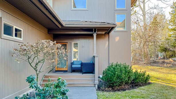 A two-story building with a covered porch, steps leading to the entrance, and a small garden area with shrubs and a tree. - Adorable Bend townhome with ideal location, kitchenette & central AC (Bend)