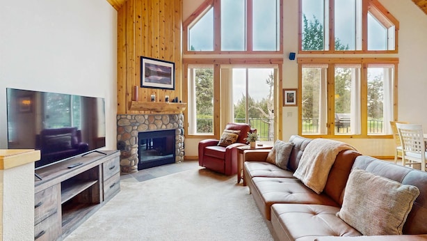 A living room with a fireplace, a television, a sofa, and large windows. - Inviting chalet with grill, patio & access to pools, hot tub, golf, tennis & gym (Redmond)