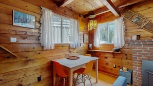 Ein Holzblock-Interieur mit Esstisch, Stühlen, Kamin und Fenster mit Vorhängen.
