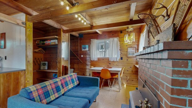 Ein gemütliches Blockhaus mit blauem Sofa, Holzwänden, einem Kamin aus Backsteinen und einem Essbereich.