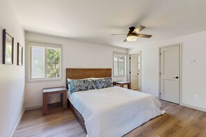 A bedroom with a wooden headboard, a bed with a white quilt, two bedside tables, a ceiling fan, and a door. - Remodeled Luxury Home with private hot tub, patio-balcony, & SHARC Passes (Sunriver)