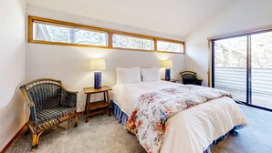 Una camera da letto con un letto, due comodini con lampade, una poltrona in vimini e una grande finestra.