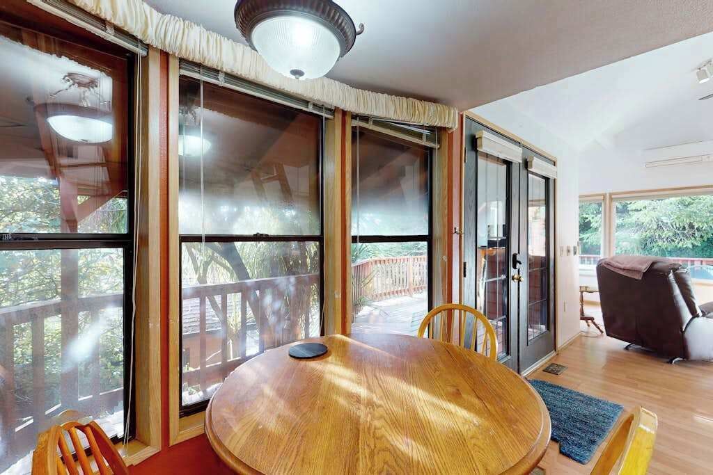 Une pièce comprenant une table à manger en bois, des chaises, un canapé et de grandes fenêtres donnant sur l’extérieur.