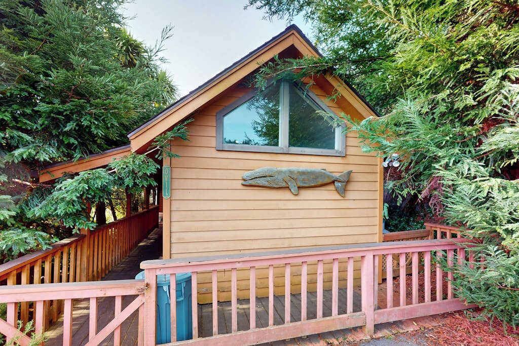 A small wooden cabin with a fish sculpture on the wall, surrounded by trees.
