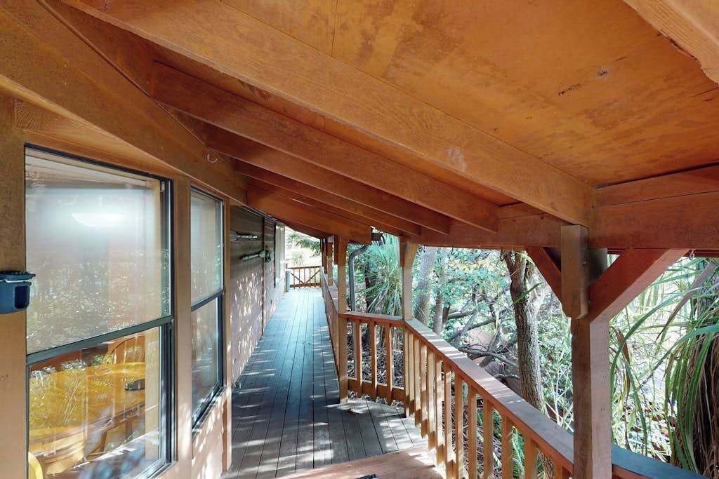 A wooden deck with a railing, large windows, and a view of trees.