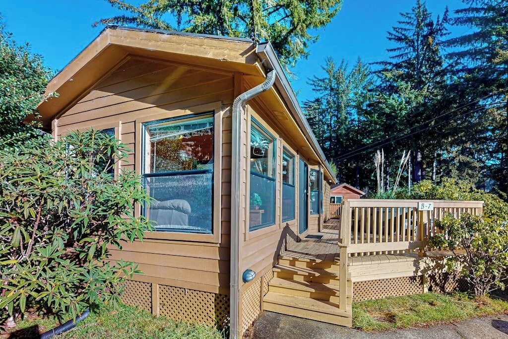 A wooden cabin with large windows, a deck, and a surrounding forest.