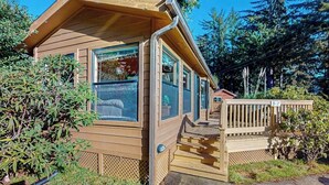 A wooden cabin with large windows, a deck, and a surrounding forest.