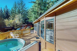 Una terraza de madera con un jacuzzi, baranda de madera y vista a zona boscosa.