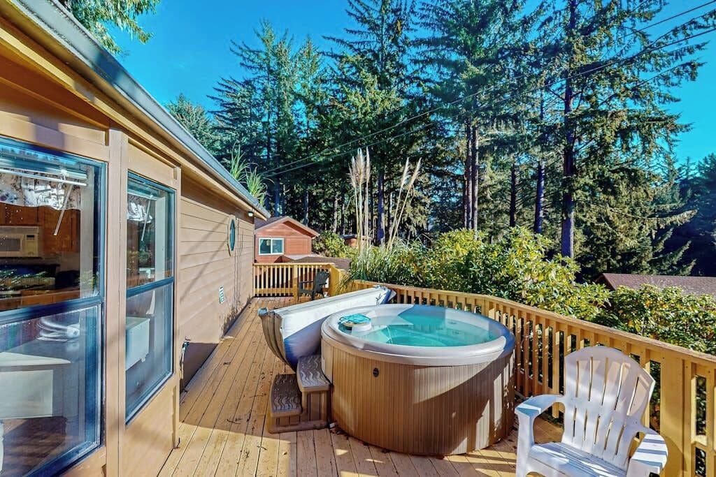 A wooden deck with a hot tub, a white chair, and a glass-enclosed room.