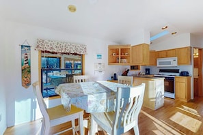 Una cocina luminosa con armarios de madera, microondas y comedor con mesa y sillas.