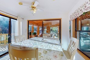 A dining area with a table set for two, a ceiling fan, and large windows with a view of the outdoors.