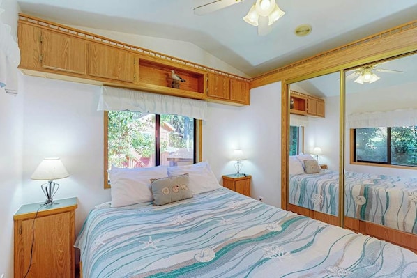 Un dormitorio con una cama, dos mesitas de noche, un ventanal, un espejo y armarios de madera.